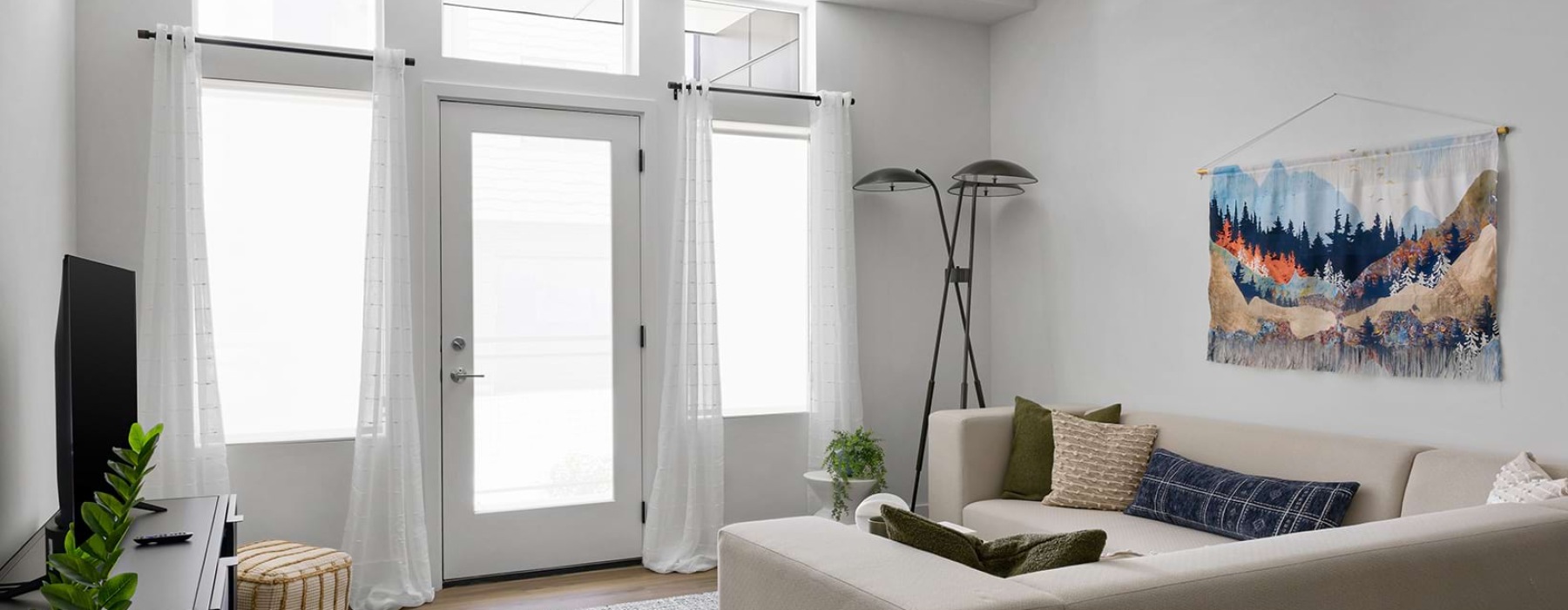 Student Apartments in Bozeman, MT, with In-Unit Washer and Dryer - boötes - Living Room With Tall Windows, Glass Door, White Curtains, Sectional Sofa, And Wall Art.