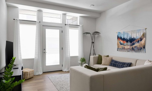 Student Apartments in Bozeman, MT, with In-Unit Washer and Dryer - boötes - Living Room With Tall Windows, Glass Door, White Curtains, Sectional Sofa, And Wall Art.