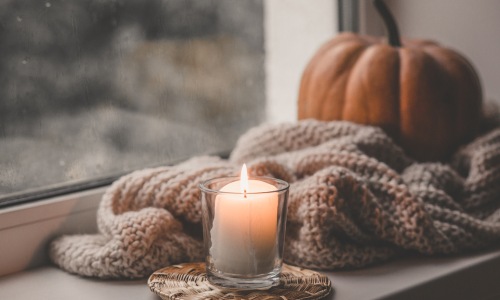 lit candlein front of a cozy throw blanket, pumpkin and window