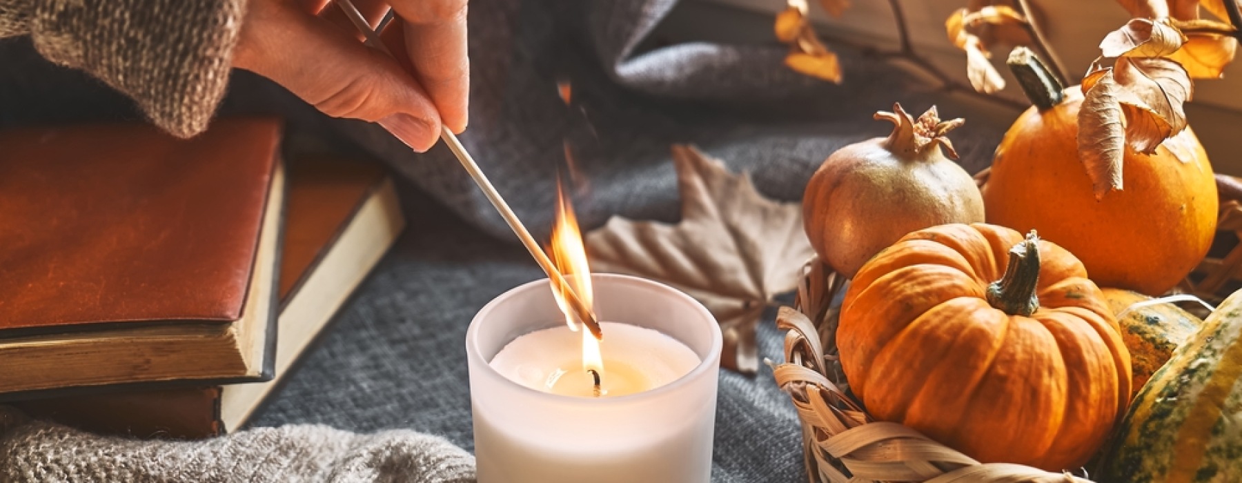 Woman lighting candle with pumpkins and books in the background